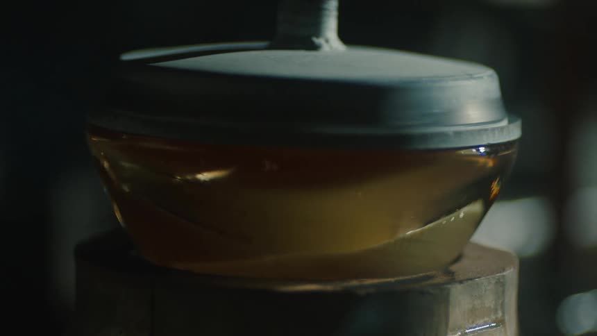 A piece of glass is being shaped and cooled on a wooden surface with smoke visible in the background capturing the glassblowing process