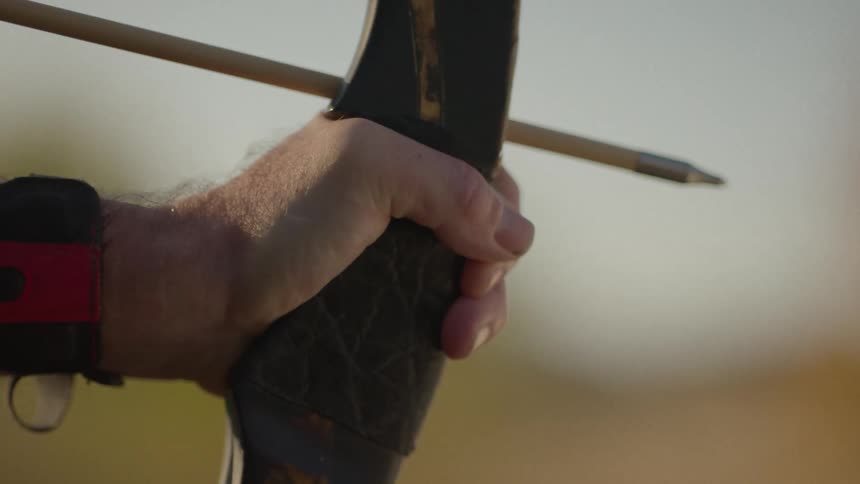 Closeup of an archers hand holding a drawn bow with an arrow ready to shoot