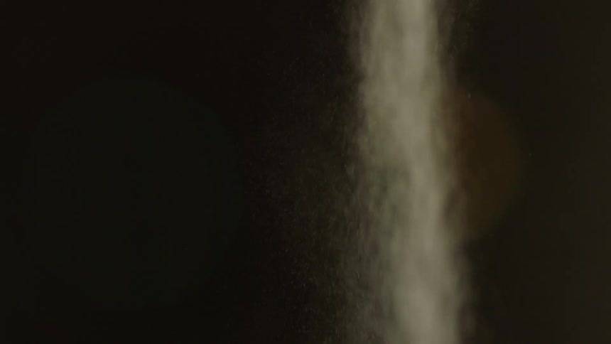 A close up of a stream of white dust or sand falling down against a dark background