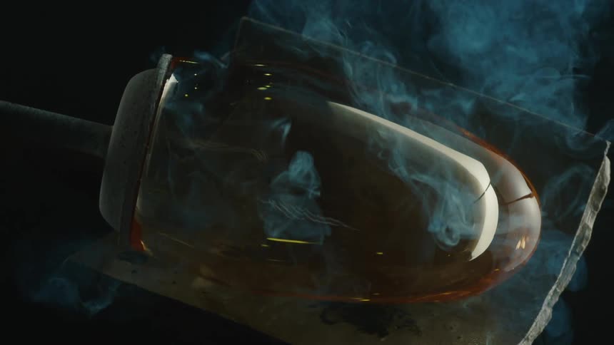 Glowing glass block being molded onto a metal surface with smoke surrounding it