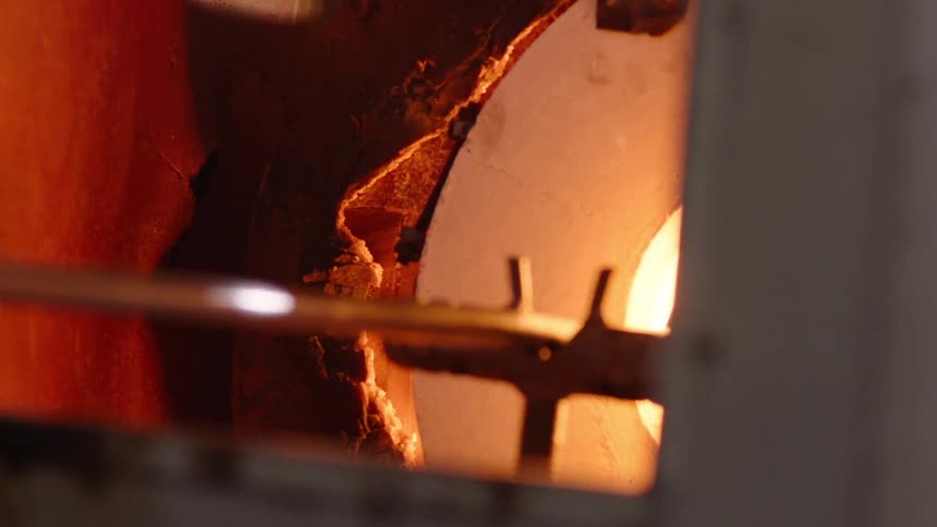 Long metal spinning hot molten glass inside a glowing hightemperature furnace