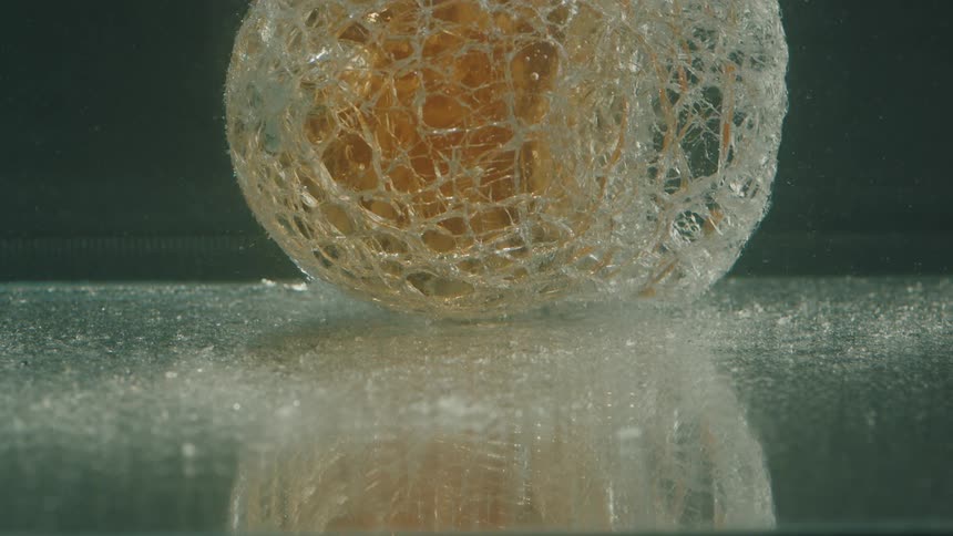 Particles rise near a golden object with a lacy outer shell sitting underwater on a reflective surface