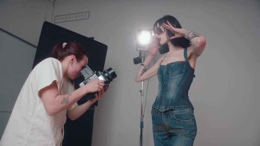 Model following instructions from a woman while being photographed in a studio