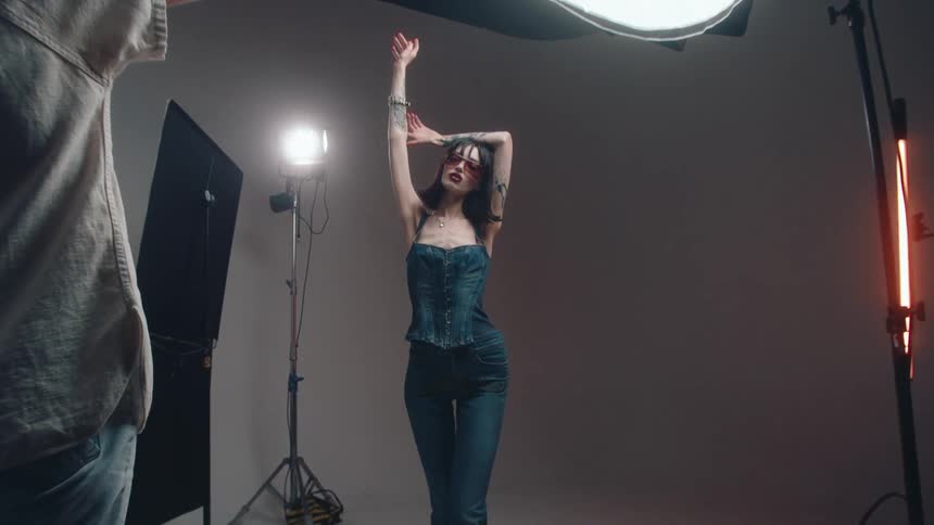 A female photographer takes pictures of a woman modeling clothes surrounded by lights