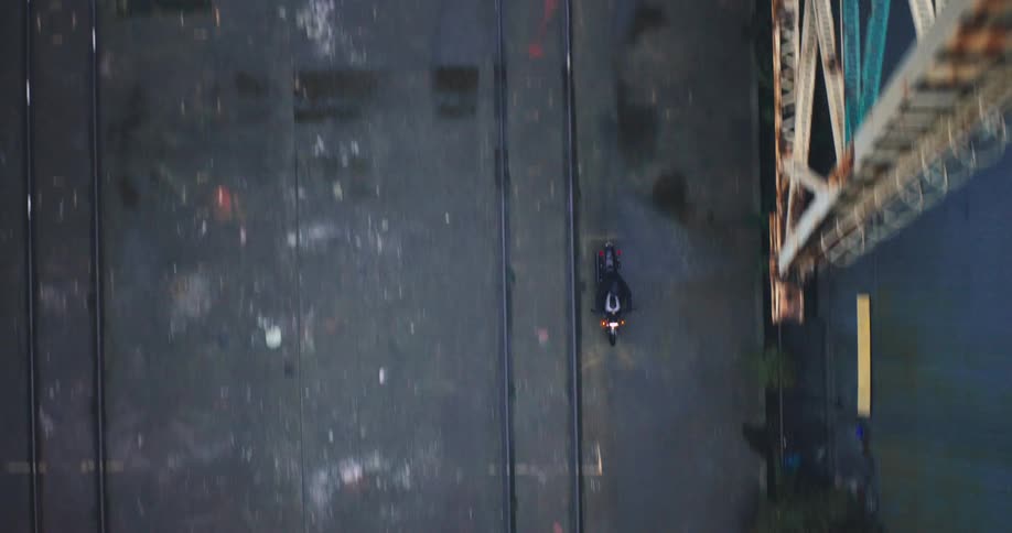 From a highangle perspective a person on a motorcycle drives on a paved surface on an industrial area