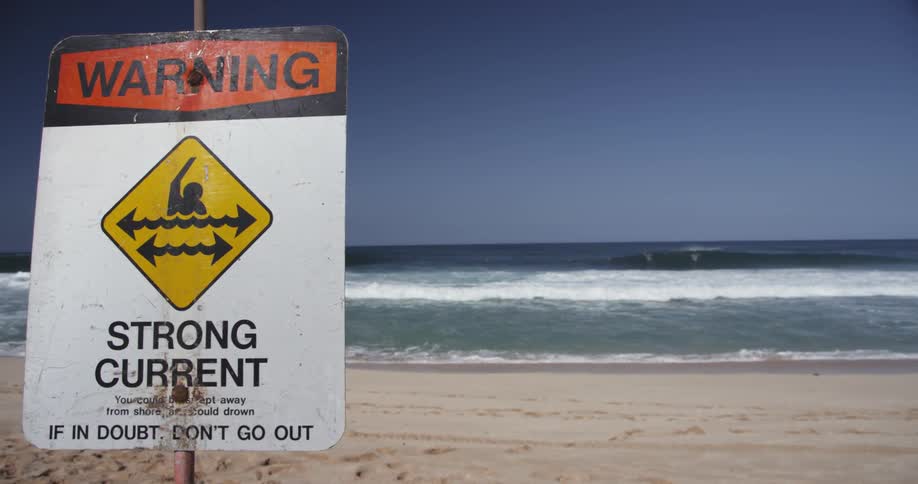Waves roll onto the shore on a beach with a warning sign