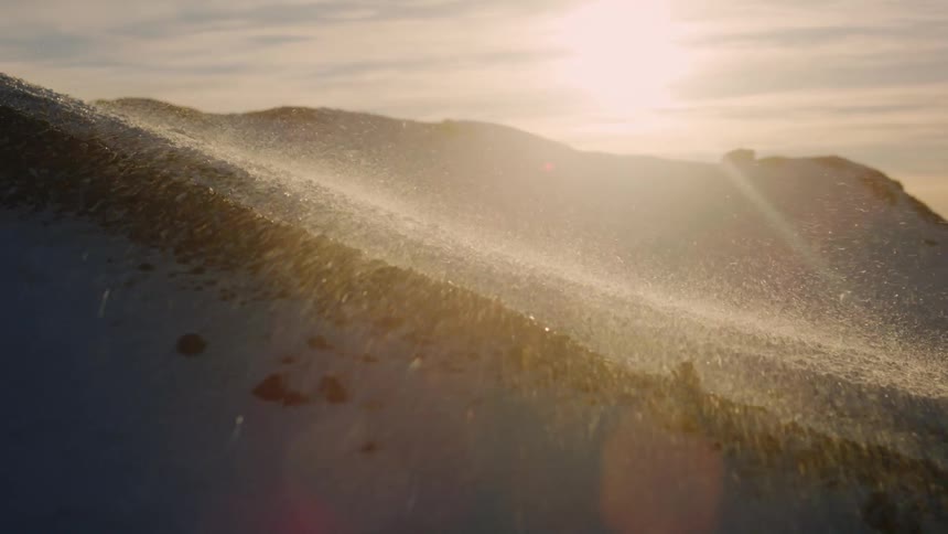 Snow flying by the force of the air on a mountain and the sun reflecting on the horizon