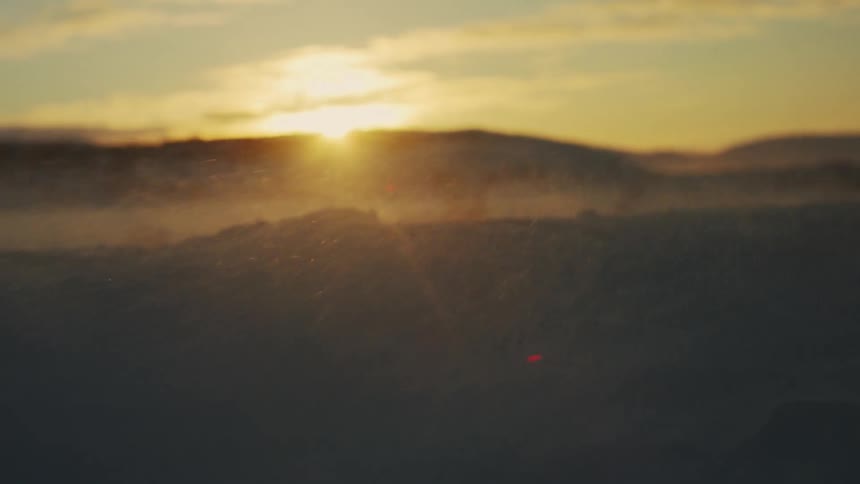Snow flying across a hilly field with the sun in the background