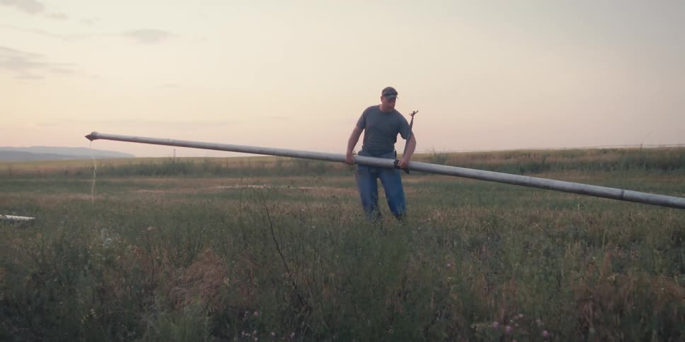Man in cap in agricultural field carrying metal pipe