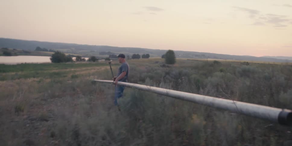 Man in cap carrying metal pipe through rural area