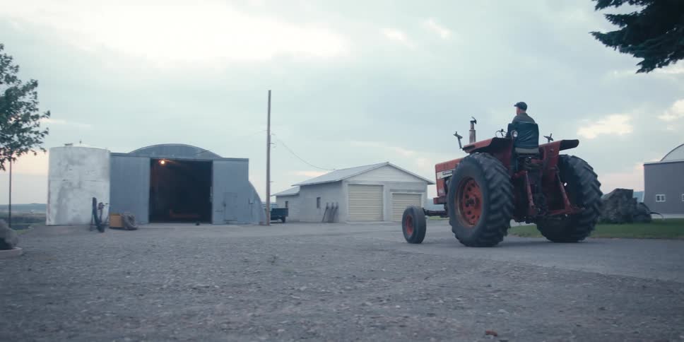 A man drives his tractor towards a barn
