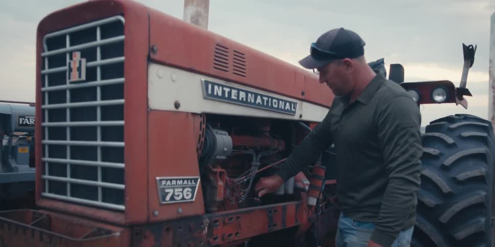 A man climbs on the tractor to repair the engine