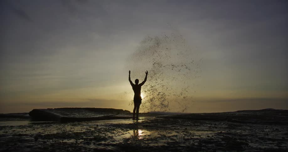 A person stands at a cliff with waves crashing before them