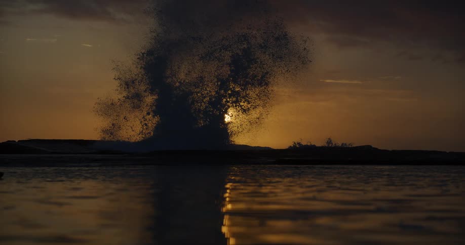 Sea water hitting a silhouette of a rock and exploding upwards with the sun in the background