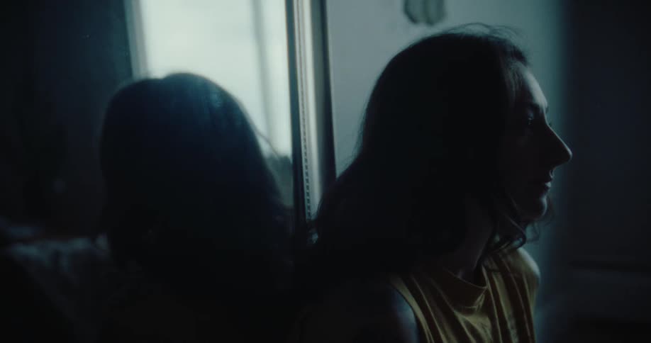 A woman sits in front of a mirror in the dark room