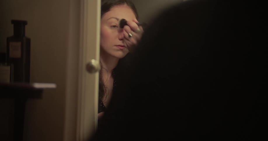 A woman applies makeup with a brush in front of a mirror in her bathroom at home