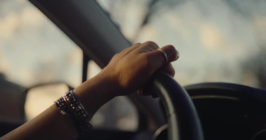 Closeup of a womans arm with a bracelet resting on the steering wheel of a moving vehicle