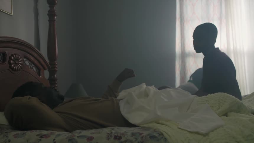 A boy walks over to a man laying in bed