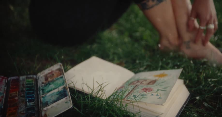 Woman sitting under a tree on the grass with an open book with a painting and snow falling