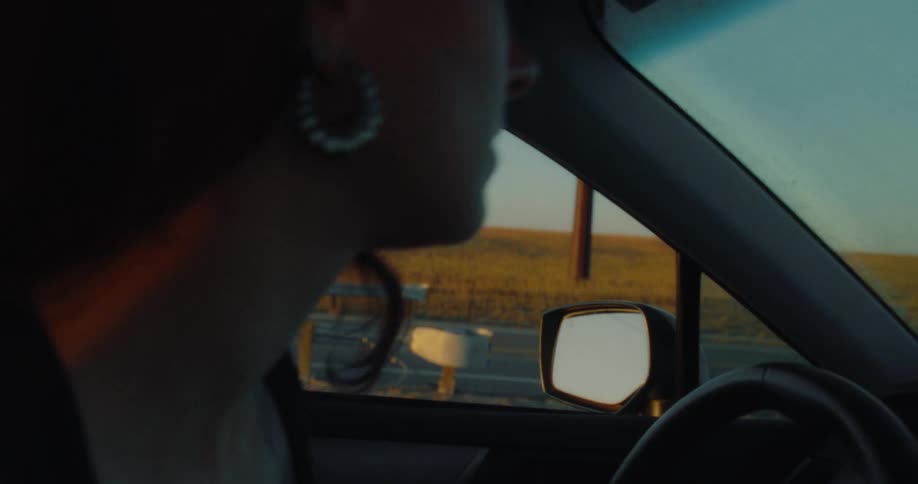 A woman brushes her teeth boards a car on the highway and starts driving on a road with a vast open landscape visible through the window