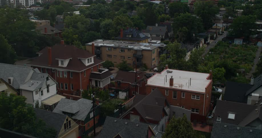 An aerial shot shows a mix of residential buildings with varying roof styles nestled among dense green treetops