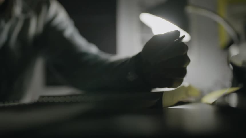 A man sits at a desk fidgeting with a pen