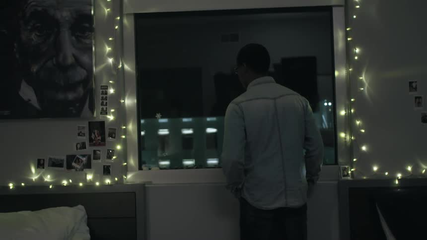 A man stands near an open window at night