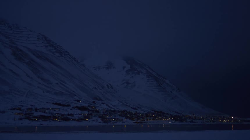 Night landscape of illuminated houses at the foot of a snowy mountain at night