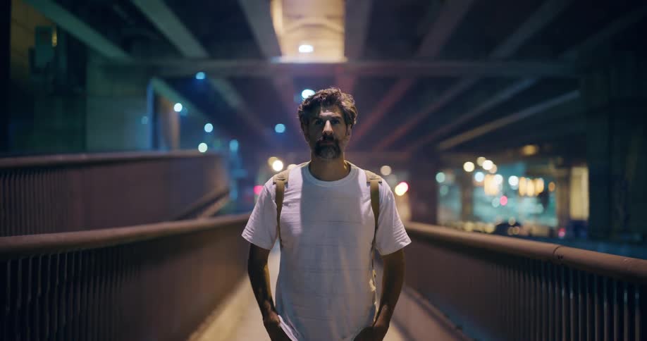 Man stands under an overpass on a walkway paralleling the highway in the evening