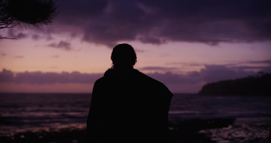 Man turns to the side while gazing out at the ocean from the beach at sunrise