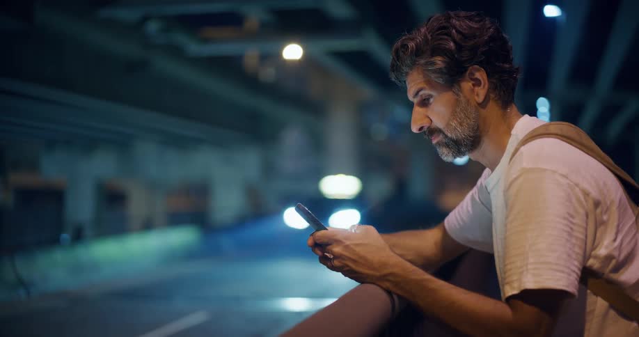 Man interacting with a smartphone next to a highway at night
