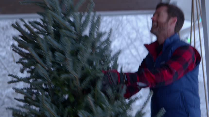 A family smiles while carrying a live christmas tree to their front porch