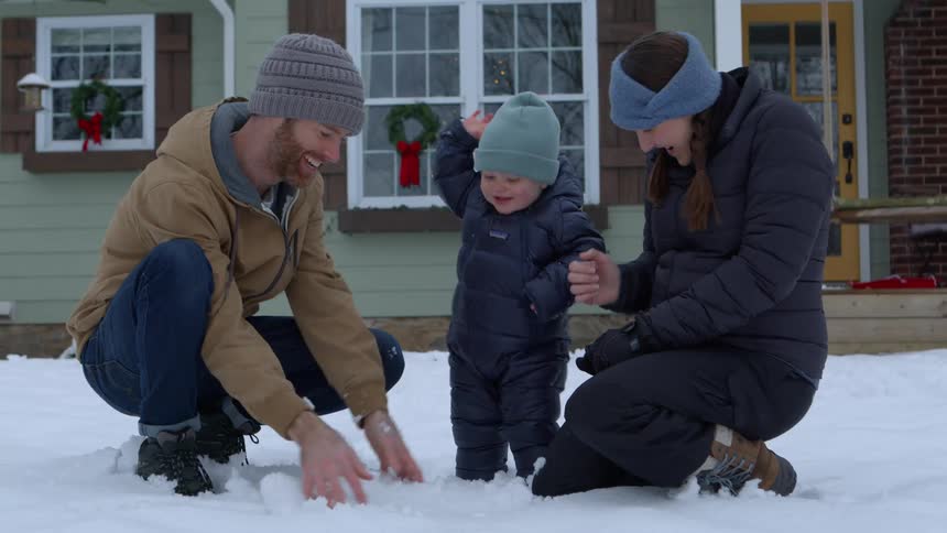 Parents play in the snow in their front yard with their child on a winter day