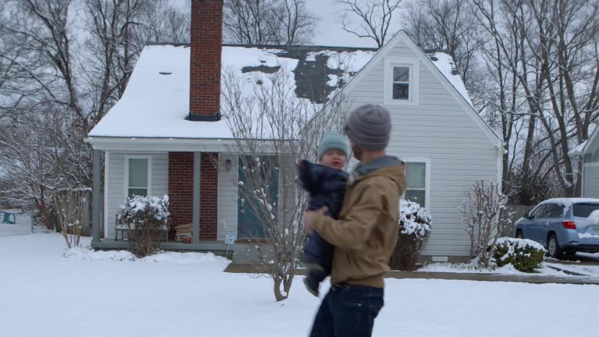 Father outdoors on a snowy day walking with his little son on his lap