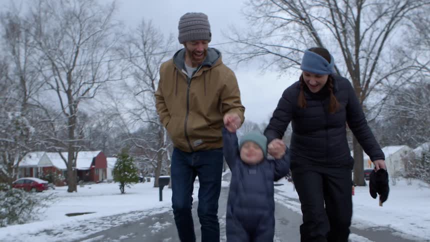 Parents walk on a residential street with their toddler on a winter day lifting the child between them
