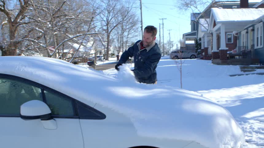 Man removing snow from vehicle windshield