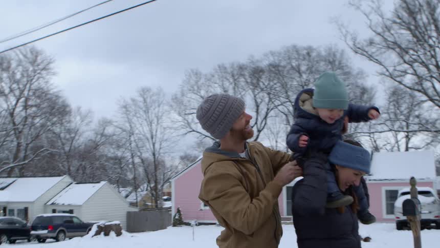 A man putting a baby on the shoulder of a woman who is in front of him and everyone is happy me wearing cold weather clothes in a region that is snowy