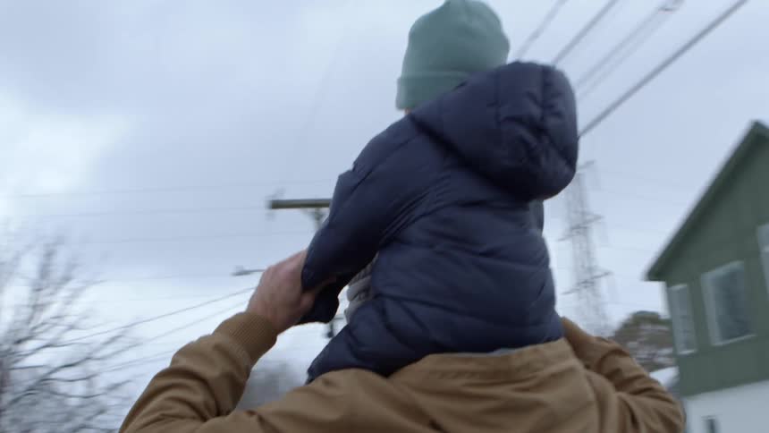 Father walking alongside his wife and carrying his son in his arms through a snowy urban neighborhood