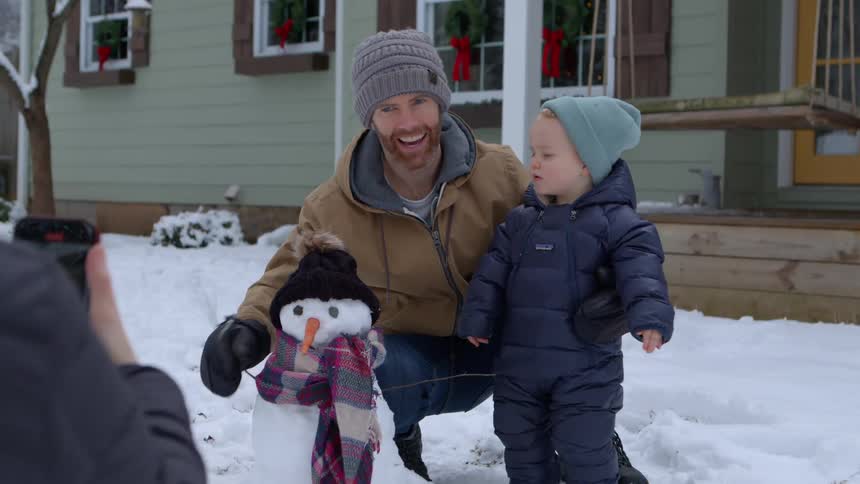 Mother taking a picture of her son next to his father and a snowman