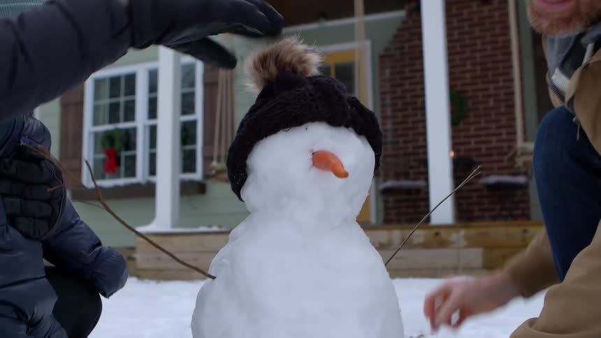 Family makes a small snowman in their front yard on a winter day