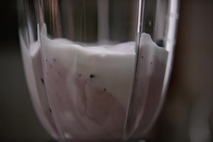 Blender combines blueberries bananas and cream to make a smoothie