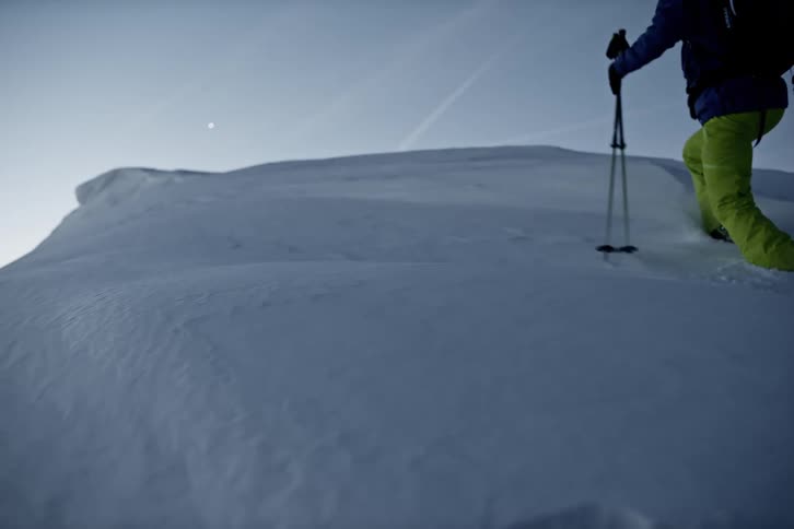 Two skiers with backpacks and poles ascend a snowy slope under a clear sky