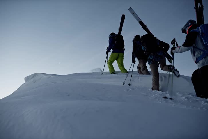 Skiers climb a snowy slope carrying their skis
