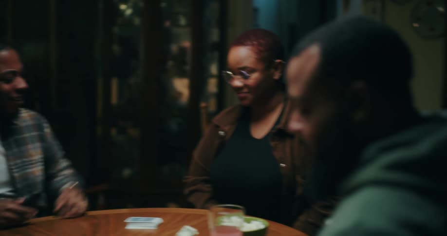 Friends play cards around a circular table in the evening
