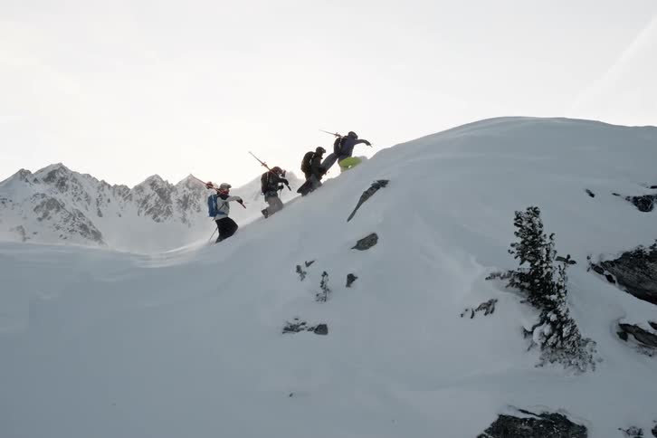 Four hikers climb a snowcovered mountain with snowboarding gear