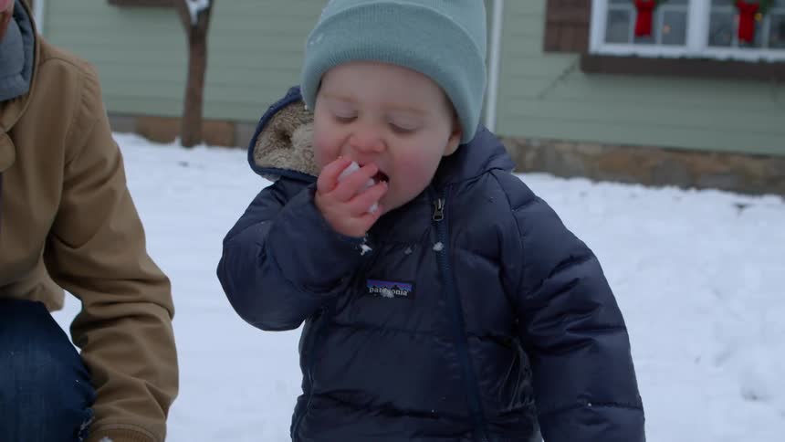 A family is playing in the snow in front of a house decorated with holiday wreaths and lights
