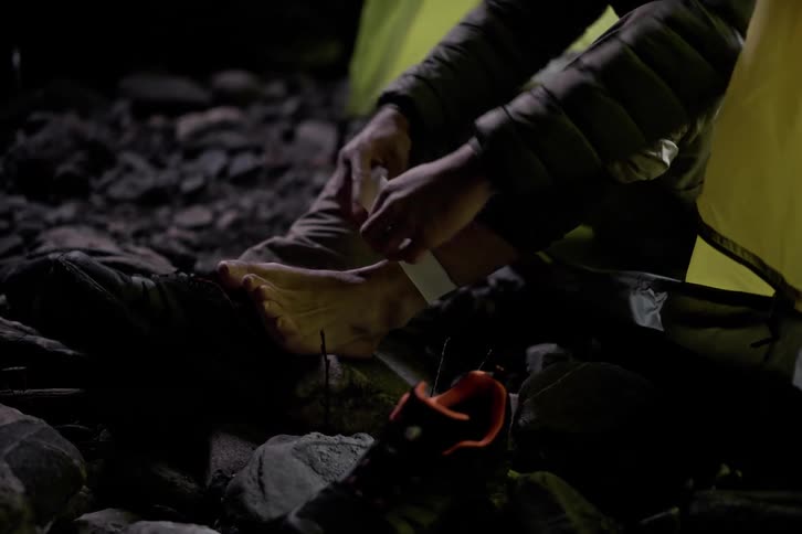 A man is taping his ankles while sitting in the tent