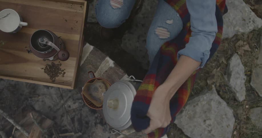 A woman pours hot water from a steaming kettle outside
