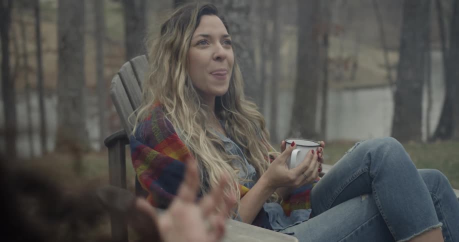 Two girls sit in chairs with mugs conversing outside
