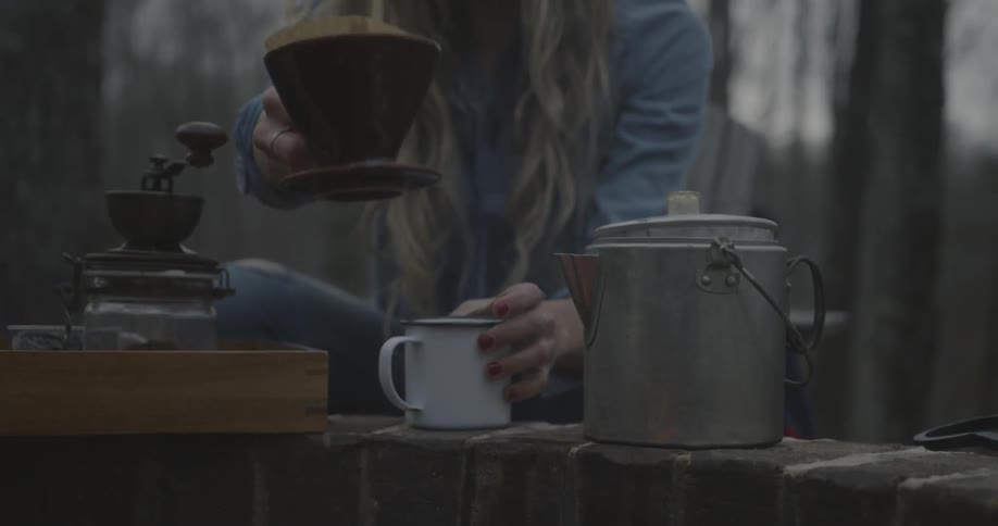 A woman makes coffee by a campfire